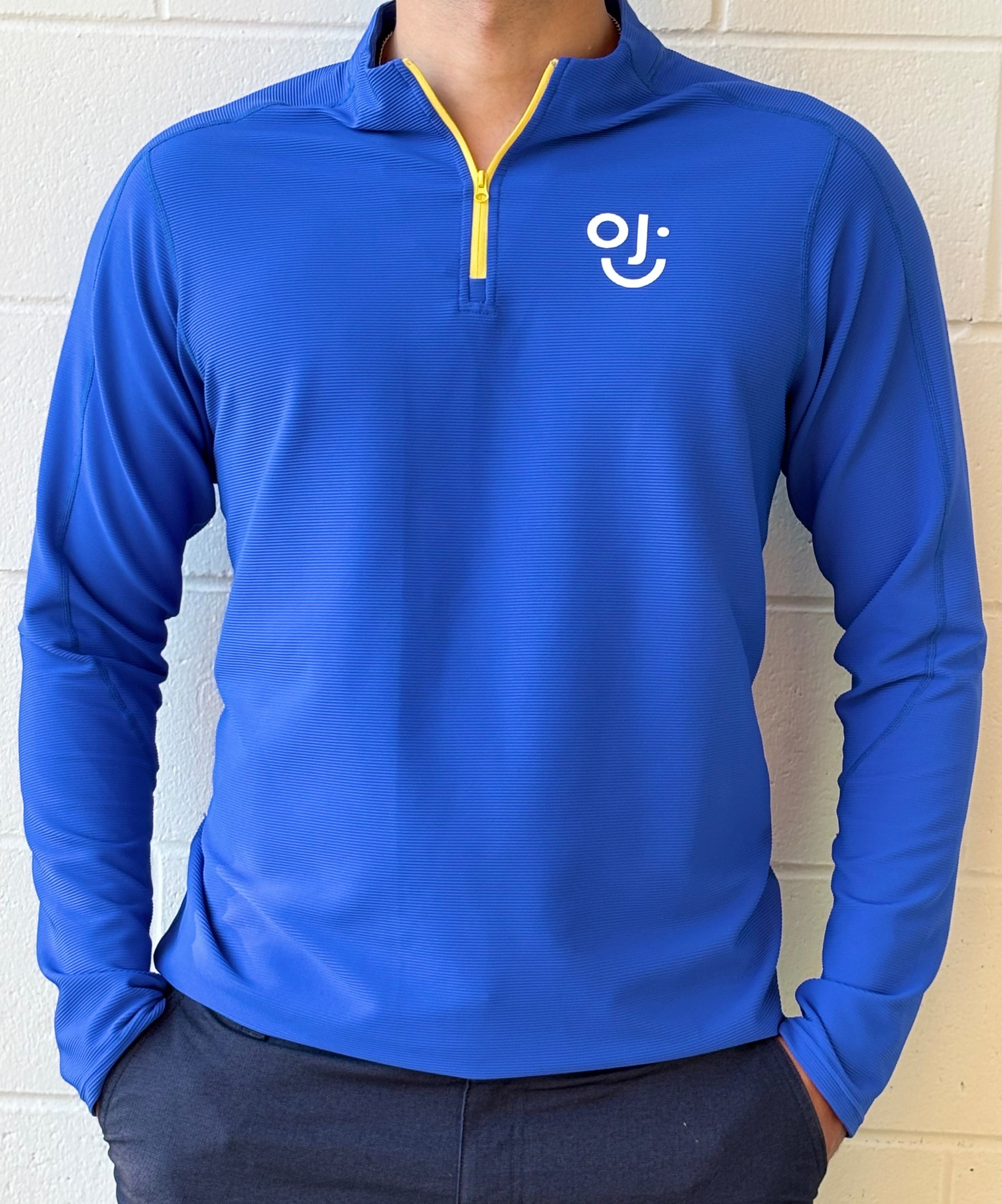 Blue long-sleeve quarter zip with OJI logo on a white brick wall background